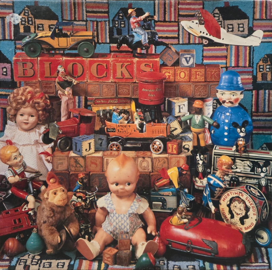 A nostalgic collection of vintage toys and dolls arranged against a colorful quilted background.