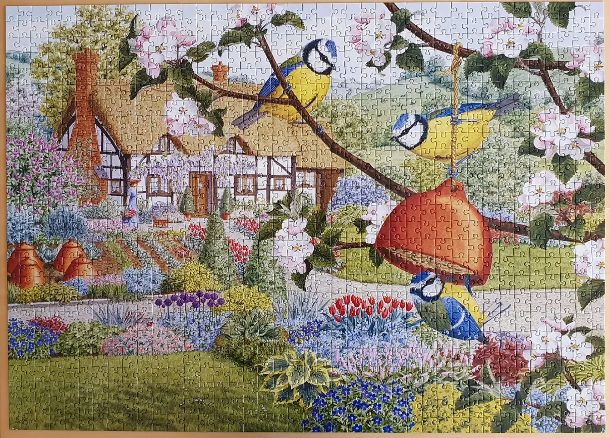 An illustration of three blue tits in a lush spring garden with a thatched cottage in the background.