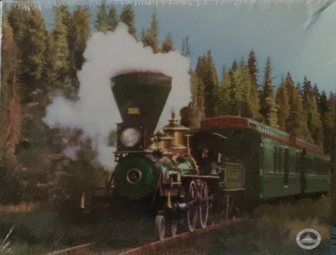 A vintage steam locomotive pulling a green passenger train through a dense evergreen forest.
