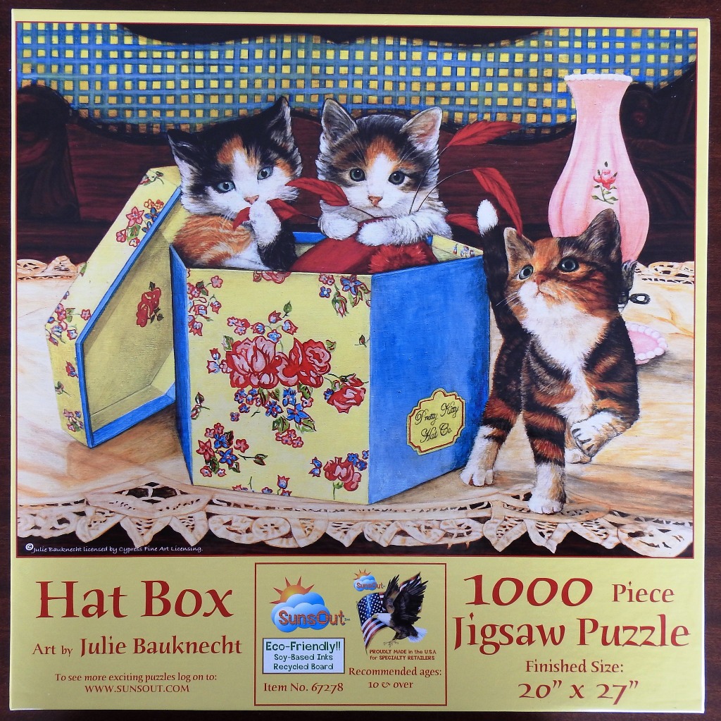 Three calico kittens playing with a floral hat box on a table.