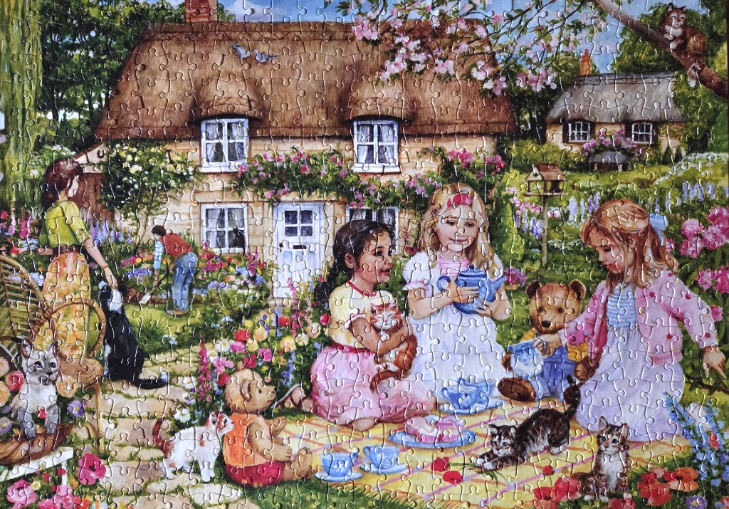 Children having a garden tea party with stuffed animals and cats in front of a thatched cottage.