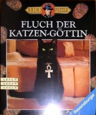 A black cat sitting in front of a tan couch wearing an Egyptian Ankh pendant.