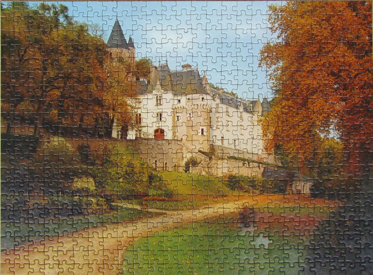 A white French castle nestled in an autumn forest with a winding dirt path in the foreground.