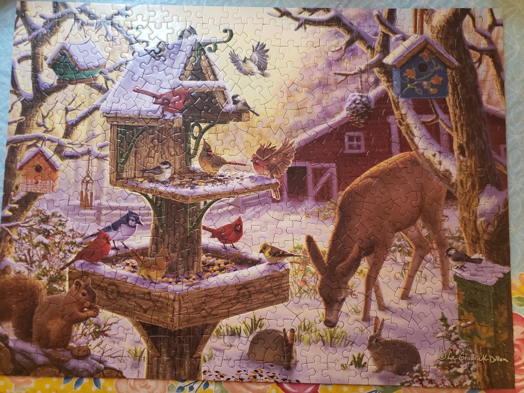 Winter scene featuring a large bird feeder surrounded by birds, a deer, and a rabbit in a snowy yard.