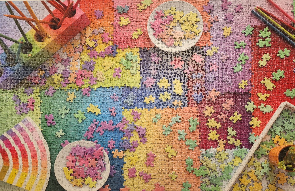 A colorful overhead view of an art studio workspace filled with pencils, paint swatches, and sorted stacks of confetti.