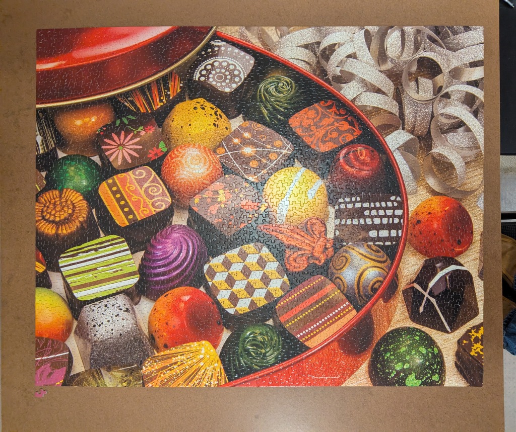 An assortment of ornate, colorful chocolates in a red tin, surrounded by festive silver ribbon.
