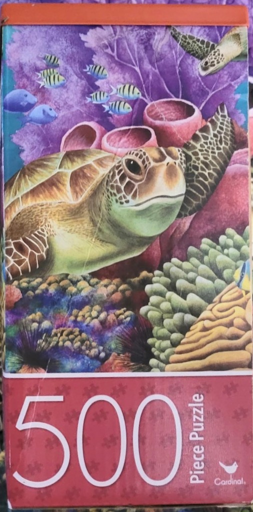 A sea turtle swimming near a colorful coral reef with schools of small fish in the background.