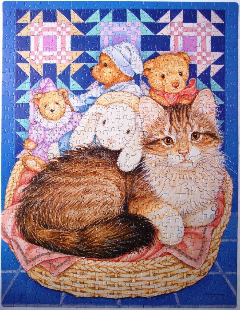 A fluffy tabby kitten sits in a basket with three stuffed toys against a blue quilt background.
