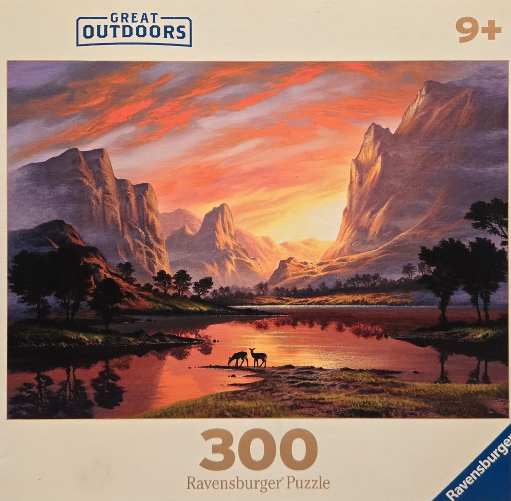 A peaceful mountain landscape at sunset with a lake and two deer in the foreground.