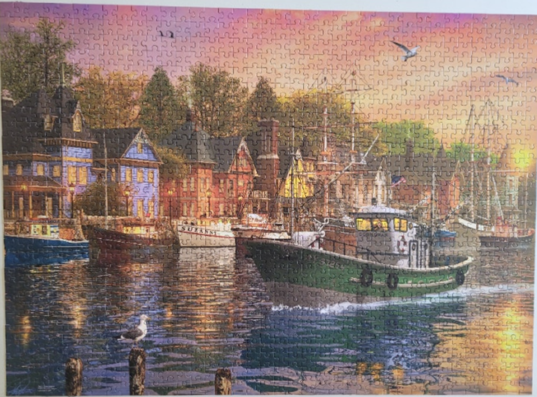 A green fishing boat moves through a harbor at sunset near a quaint coastal town.