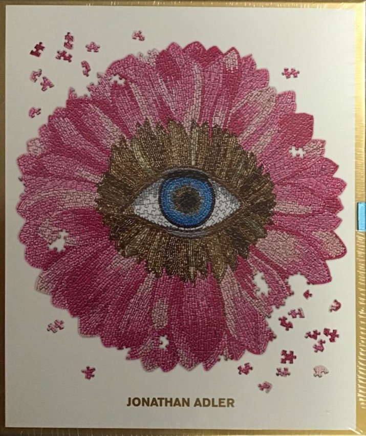 A stylized pink flower with a realistic human eye in the center, surrounded by floating puzzle piece shapes.