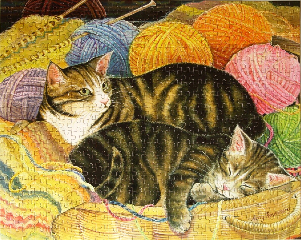Two tabby cats resting among balls of colorful yarn in a woven basket