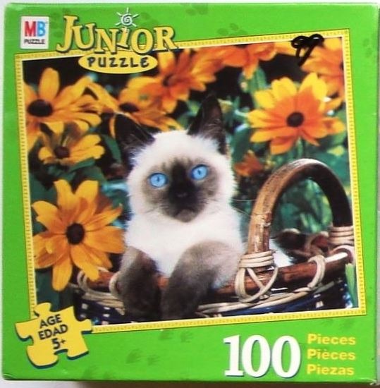 A Siamese kitten with bright blue eyes sitting in a wicker basket surrounded by yellow black-eyed Susan flowers.