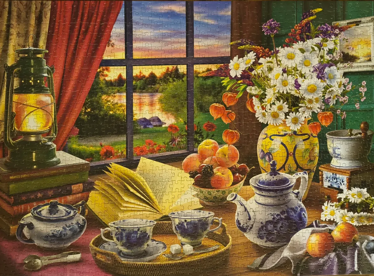 A cozy window view with a lit lantern, a bouquet of wildflowers, and a tea set on a table at sunset.