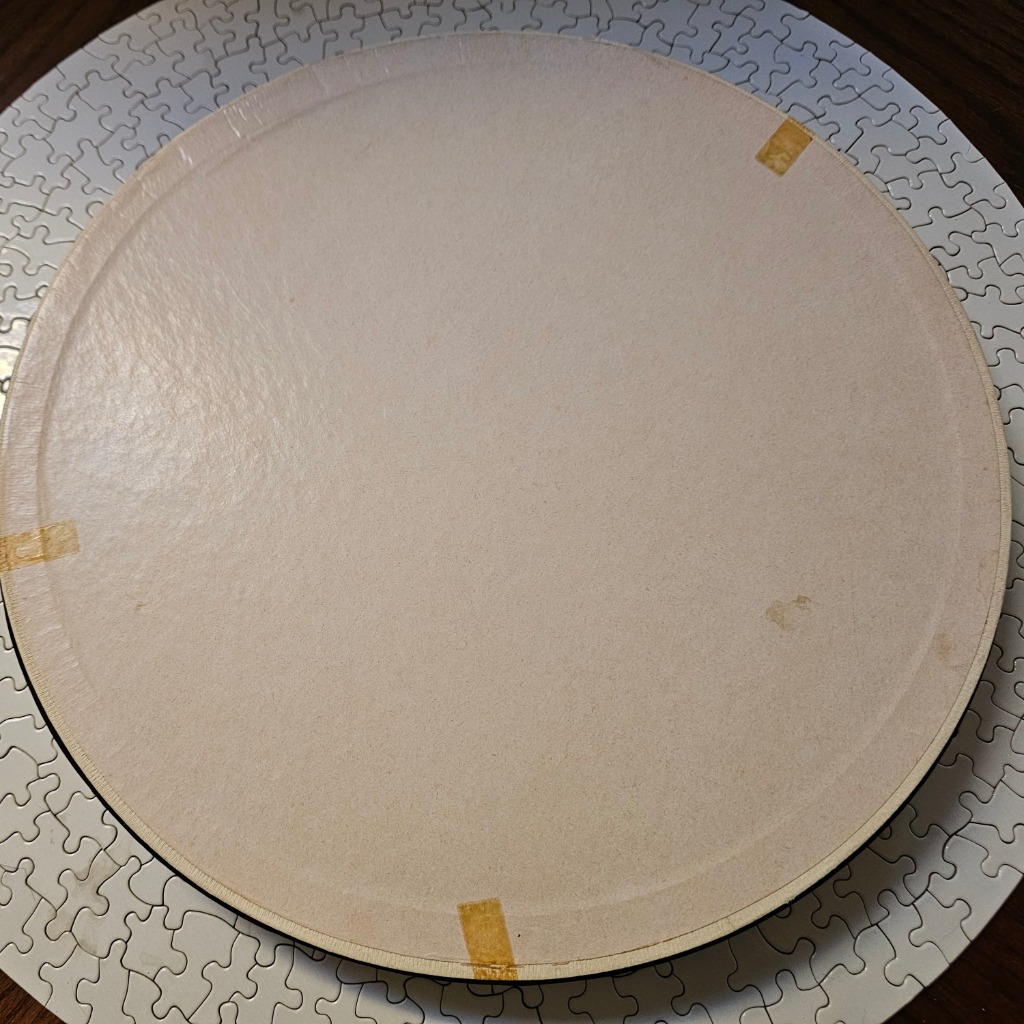 A blank, circular off-white surface placed over a background of white jigsaw pieces.