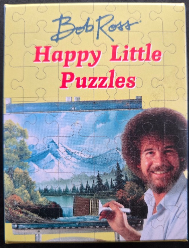 Bob Ross smiling beside a landscape painting of mountains and a lake