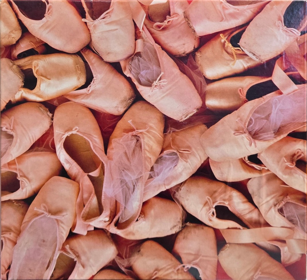 A dense pile of worn pink ballet pointe shoes viewed from above.