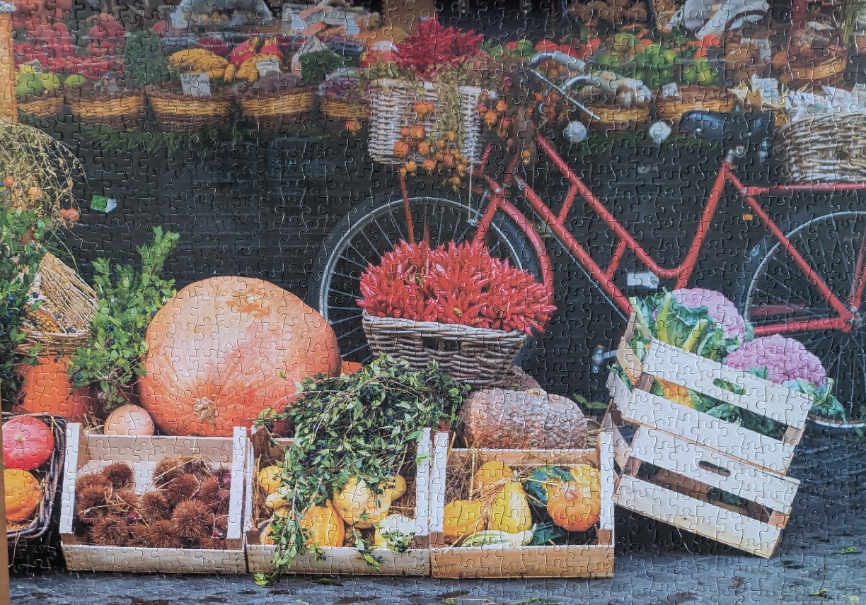A red bicycle leaning against a wall behind baskets and crates of fresh autumn produce.