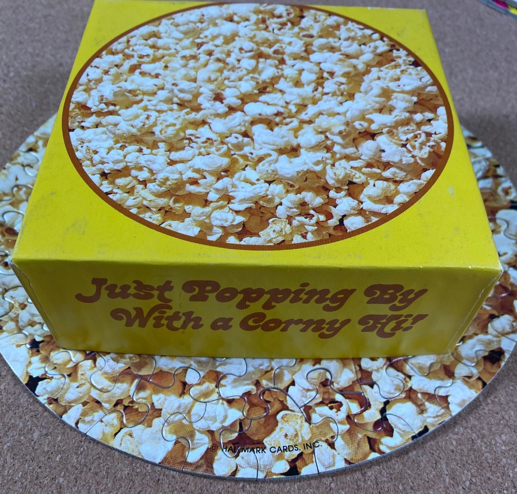 A close-up of a circular popcorn image on a yellow background with the text 'Just Popping By With a Corny Hi!'
