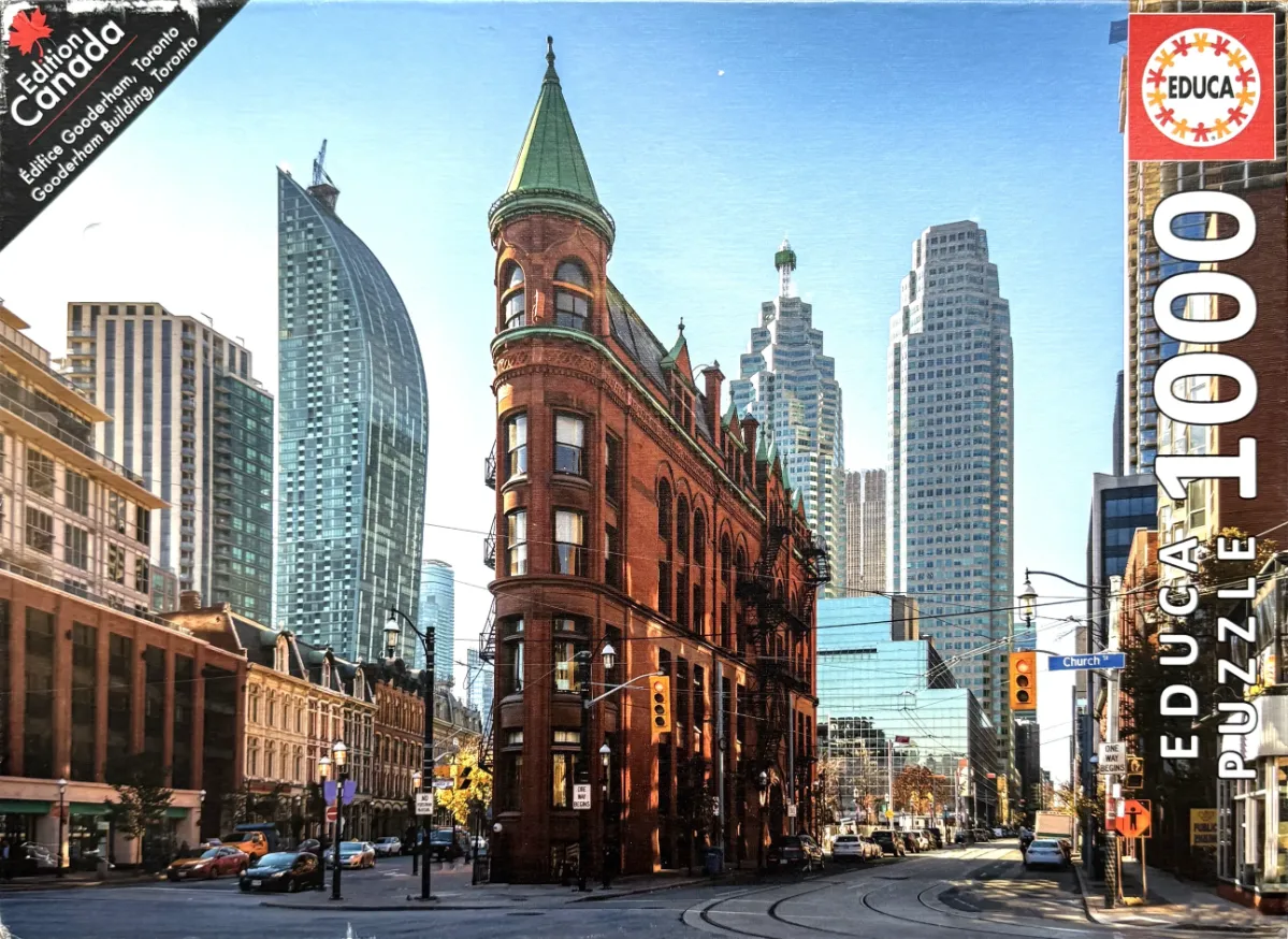 The historic Gooderham Building in Toronto surrounded by modern skyscrapers under a clear blue sky.