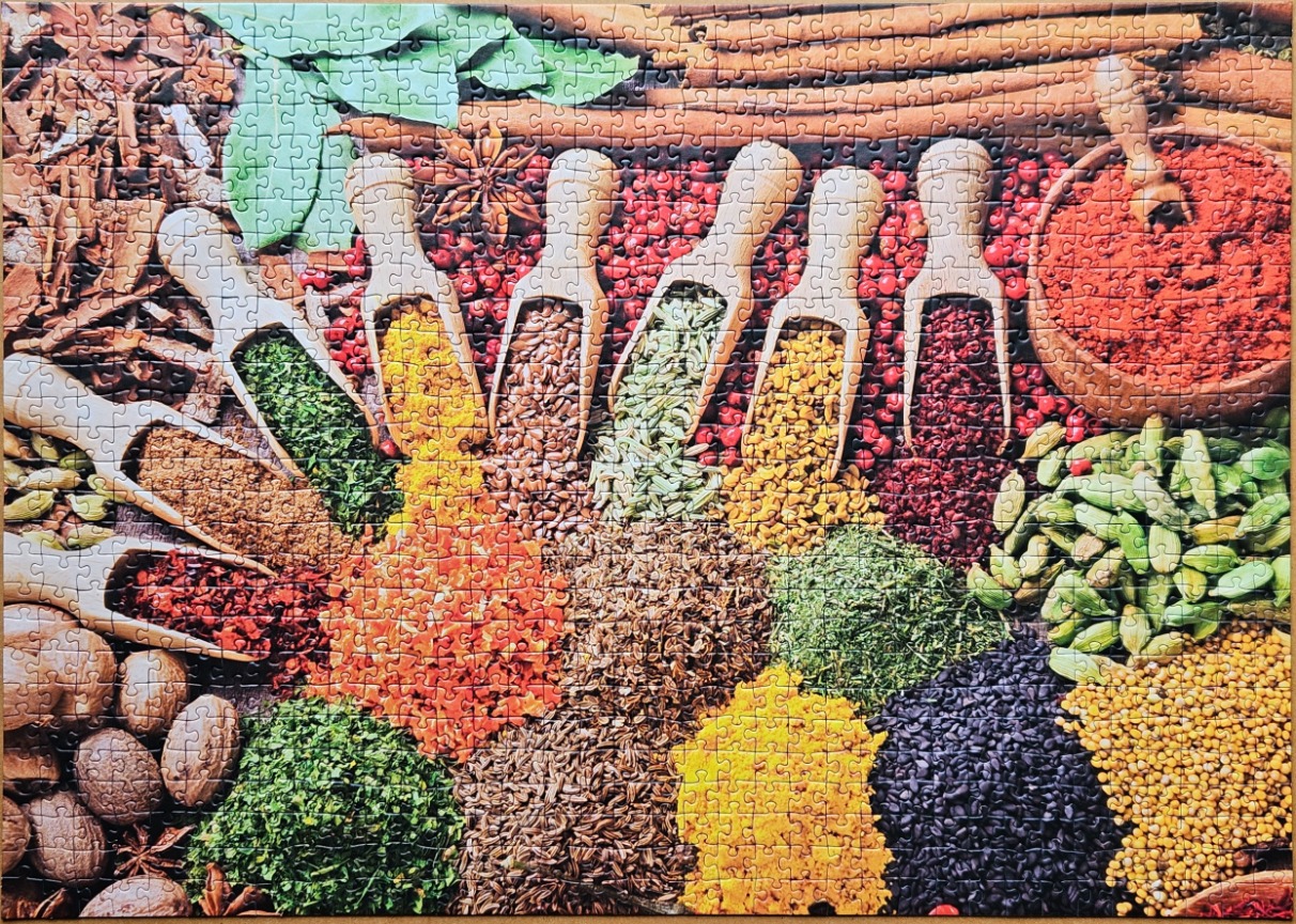 Top-down view of various spices, herbs, and seeds arranged in wooden scoops and piles.