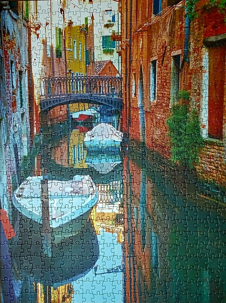 A narrow canal scene in Venice featuring a small boat, an arched bridge, and weathered, colorful buildings.