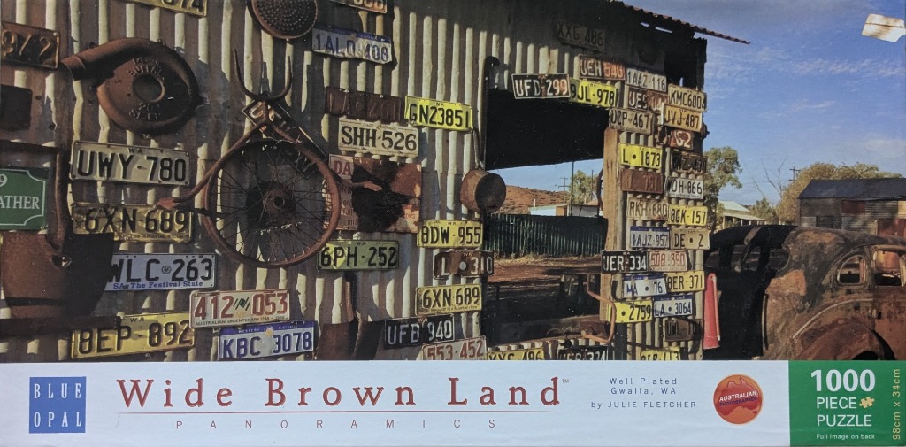 A rustic corrugated metal shed wall covered in various old Australian license plates and vintage metal relics.