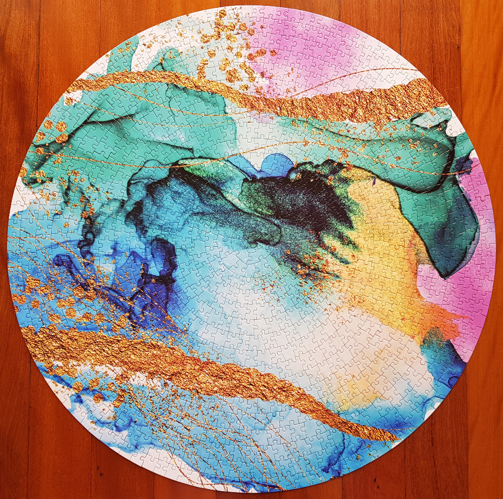 Abstract circular artwork featuring flowing teal, blue, and violet ink washes accented by textured metallic gold leaf.