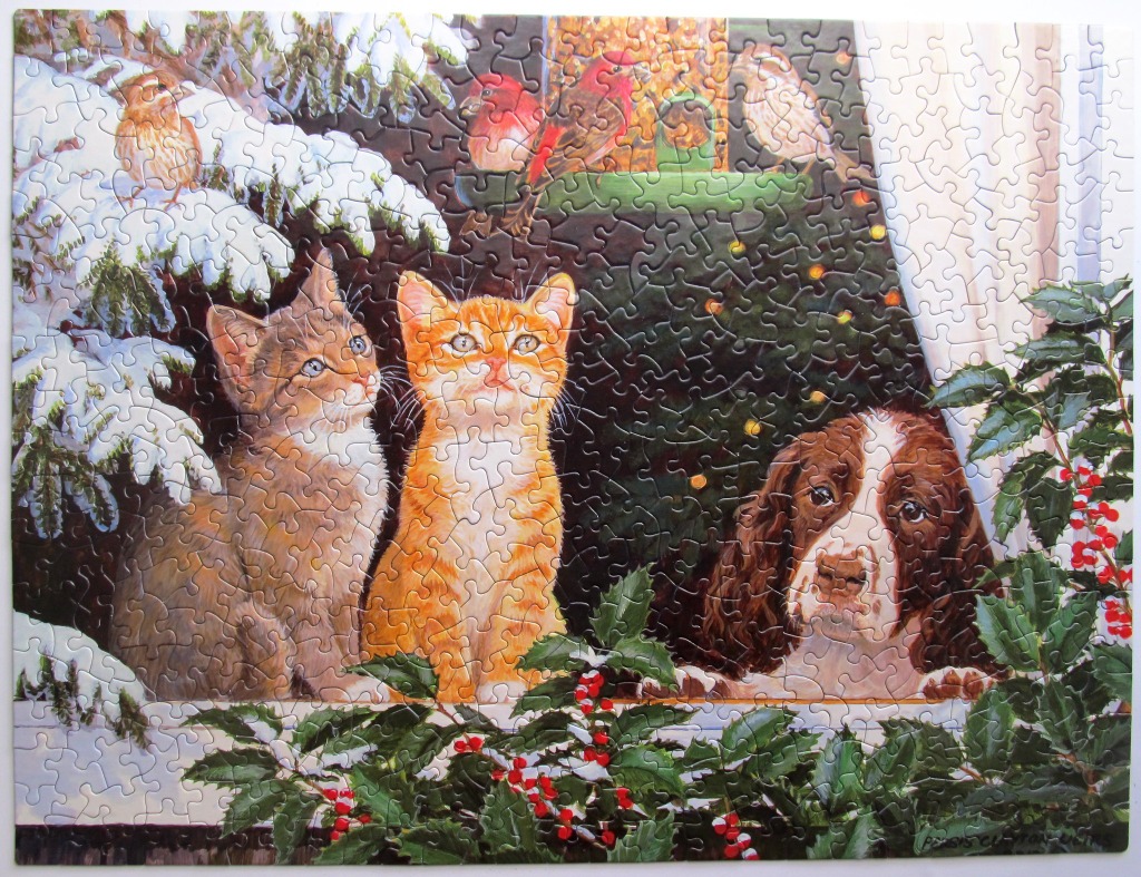 Two kittens and a spaniel watching birds from a snowy window sill.