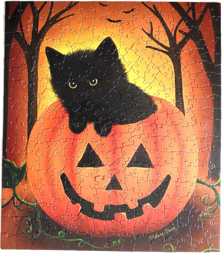 A black cat sitting atop a jack-o'-lantern against an orange sunset background.
