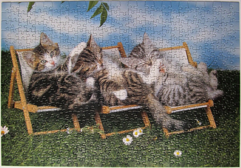 Three tabby kittens lounging together on a wooden beach chair in a grassy field.
