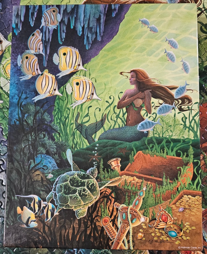 Illustration of a mermaid swimming near a sea turtle and a sunken treasure chest underwater.
