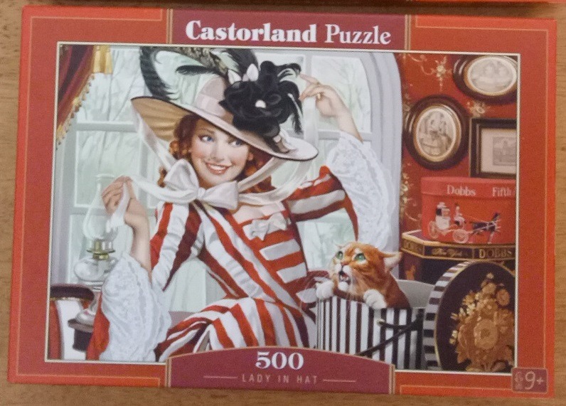 A woman in a red-and-white striped dress and a large hat with a ginger cat peeking out of a hat box.