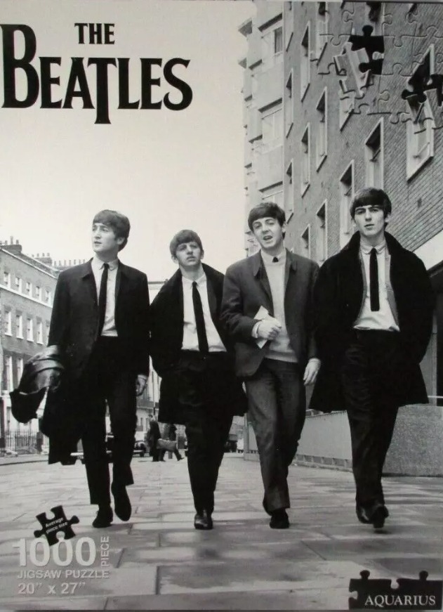 Black and white photograph of The Beatles walking in a line along a city sidewalk.