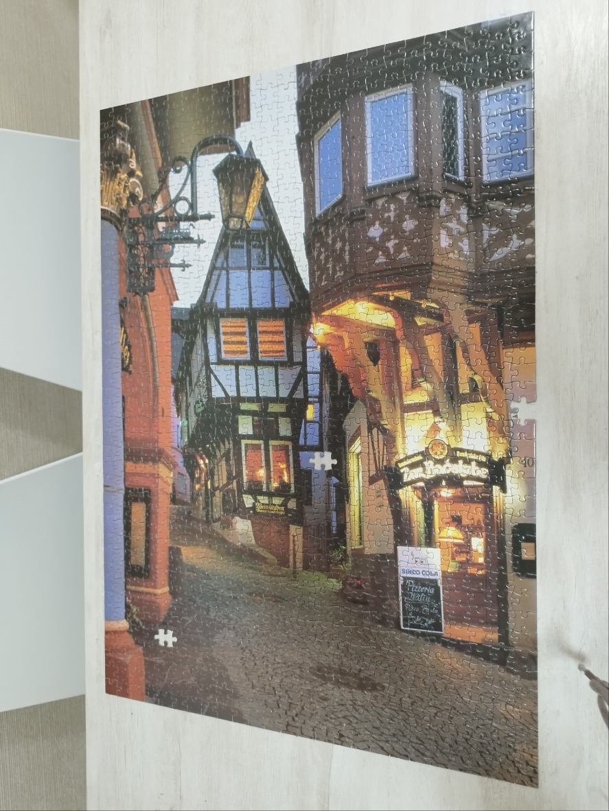 A charming cobblestone street at dusk featuring timber-framed medieval buildings and glowing shop lights.