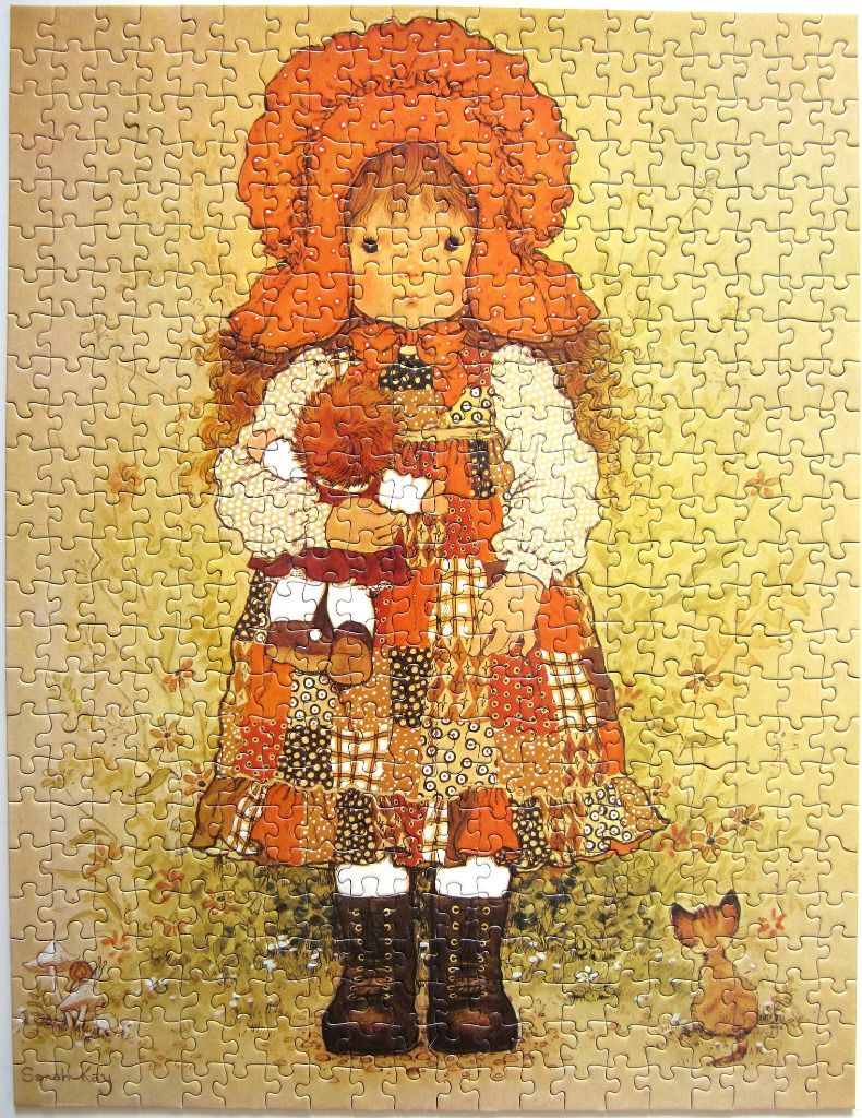 An illustration of a young girl in a large orange bonnet holding a doll, standing in a meadow with a small cat.