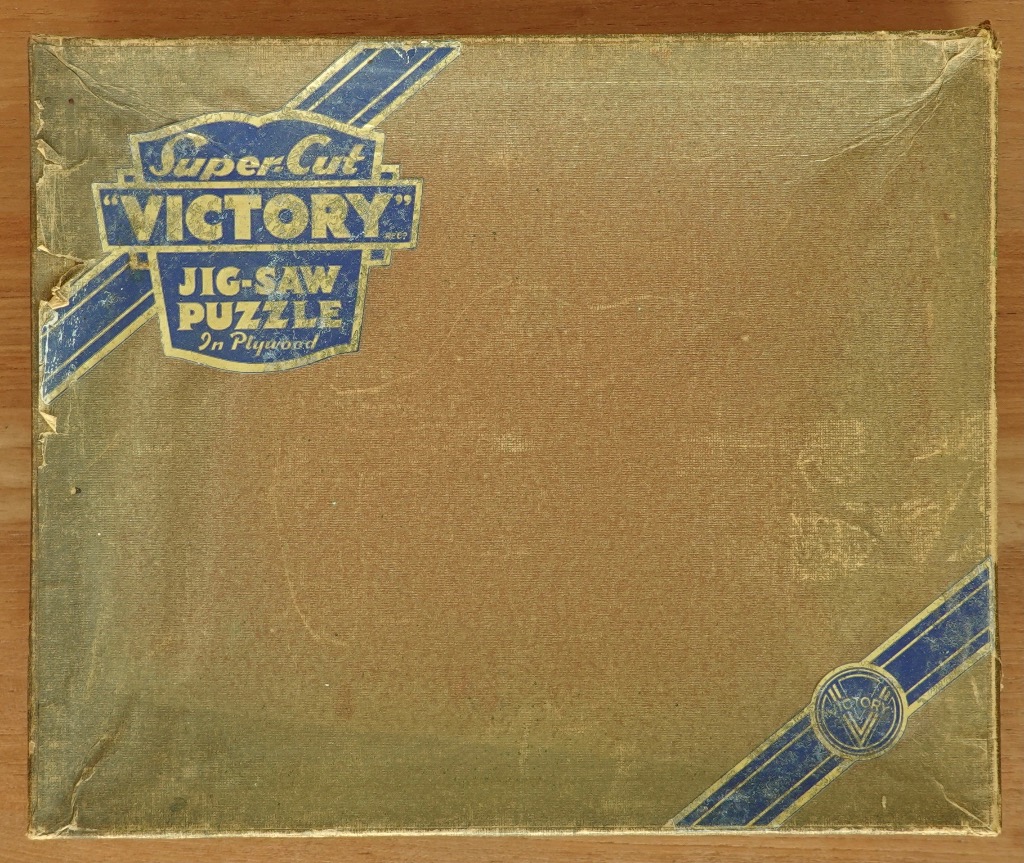 Vintage gold-toned rectangular box with a blue crest logo in the upper left corner and a circular emblem in the lower right.