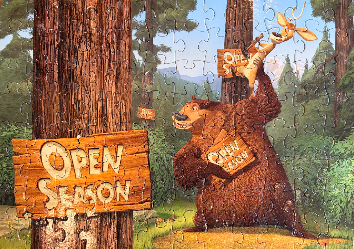 Boog the bear and Elliot the deer standing in a forest with Open Season signs.