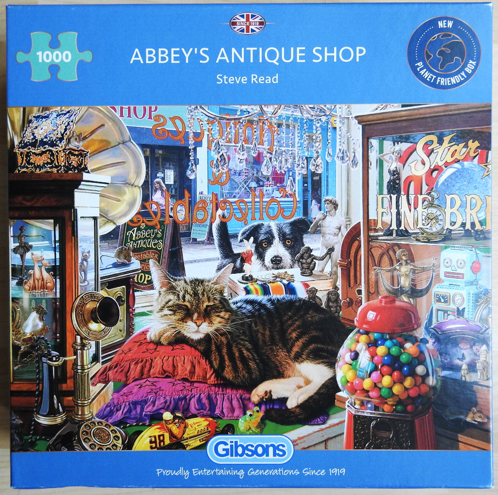 A tabby cat sleeping on purple and red pillows inside an antique shop surrounded by vintage trinkets and toys.