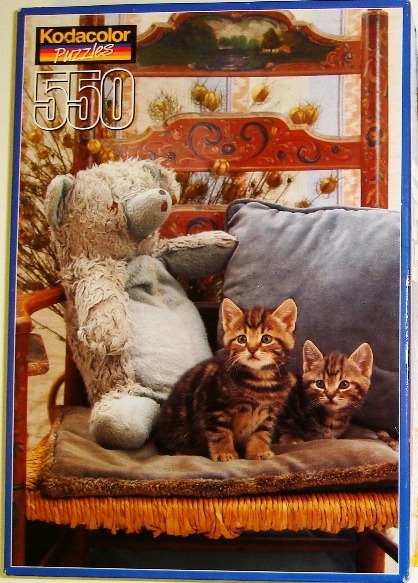 Two tabby kittens sitting on a cushioned chair next to a teddy bear