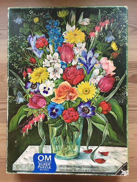 An oil painting of a vibrant, multi-colored bouquet of spring flowers in a glass vase on a marble ledge.