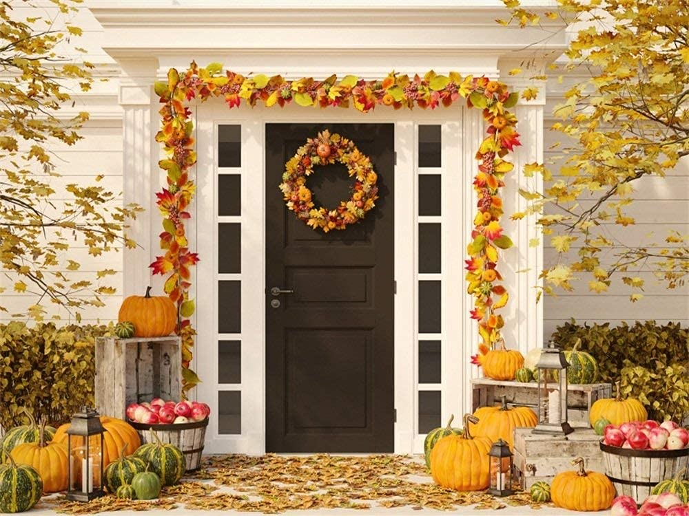 A black front door decorated with an autumn wreath and fall foliage, surrounded by pumpkins and crates of apples.
