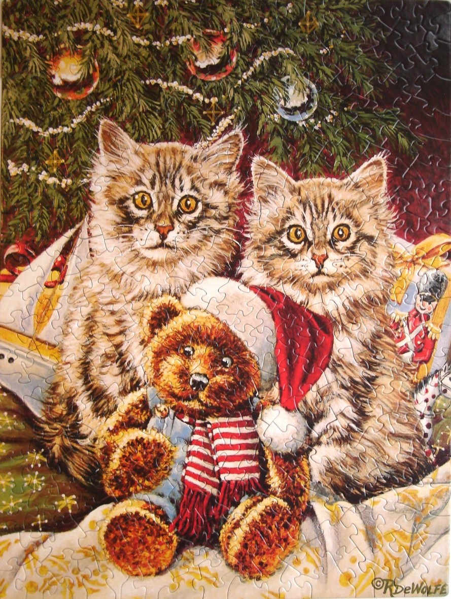 Two fluffy tabby kittens sitting in front of a Christmas tree with a teddy bear.