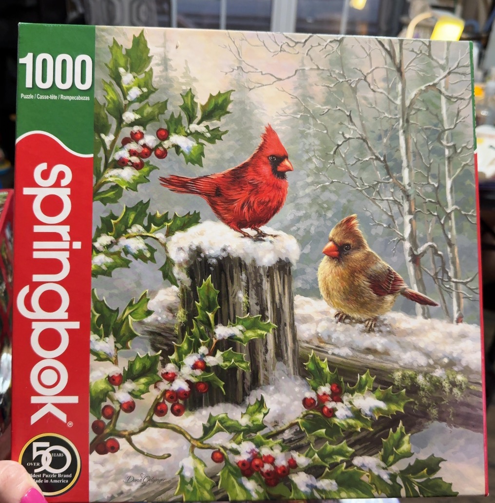 Two cardinals perched on a snow-covered fence post surrounded by holly branches in a winter forest.