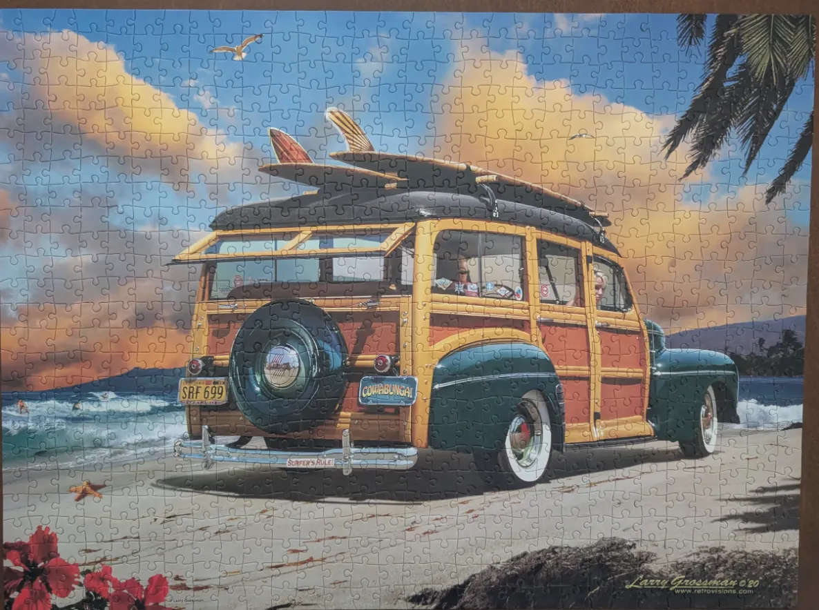 A vintage wooden station wagon parked on a sandy beach at sunset, topped with surfboards.