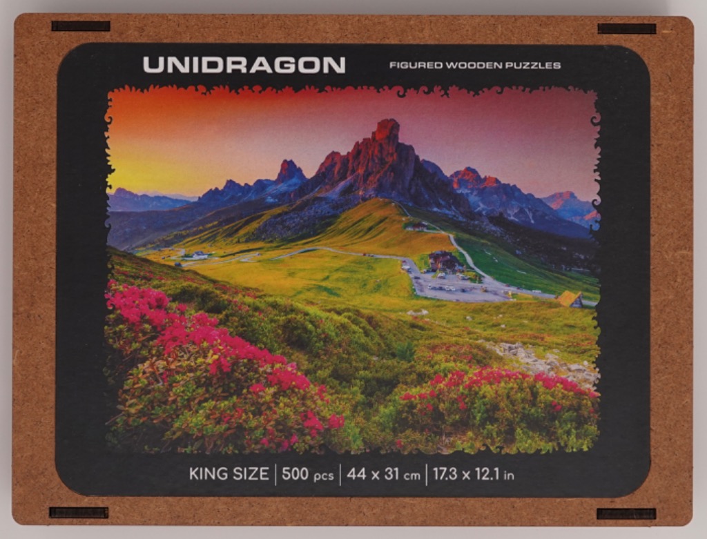 Alpine landscape with jagged mountains, rolling green meadows, and bright pink flowers at sunrise.