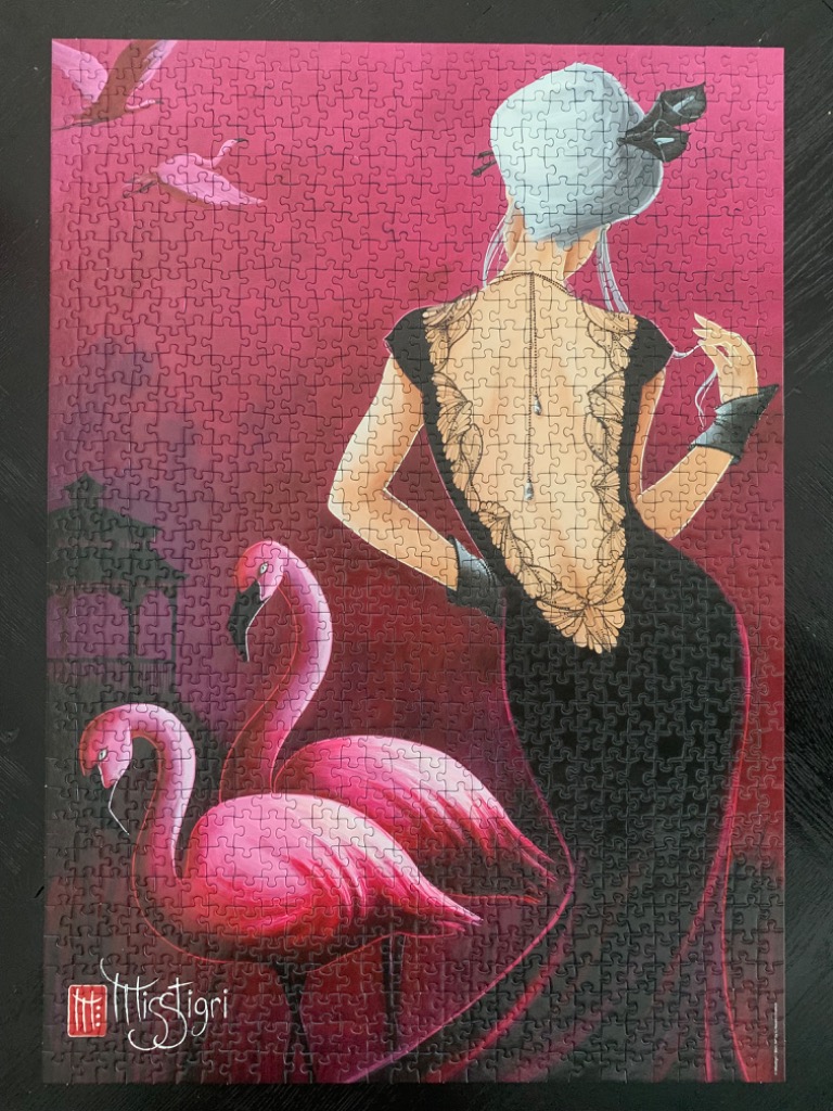 A stylish woman in a backless dress stands beside two flamingos against a vibrant magenta background.