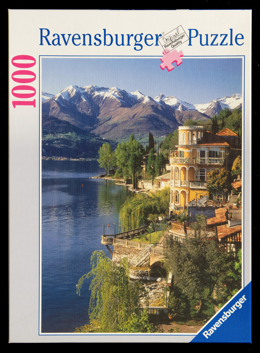 Scenic view of an Italian villa on a lake with snow-capped mountains in the background.