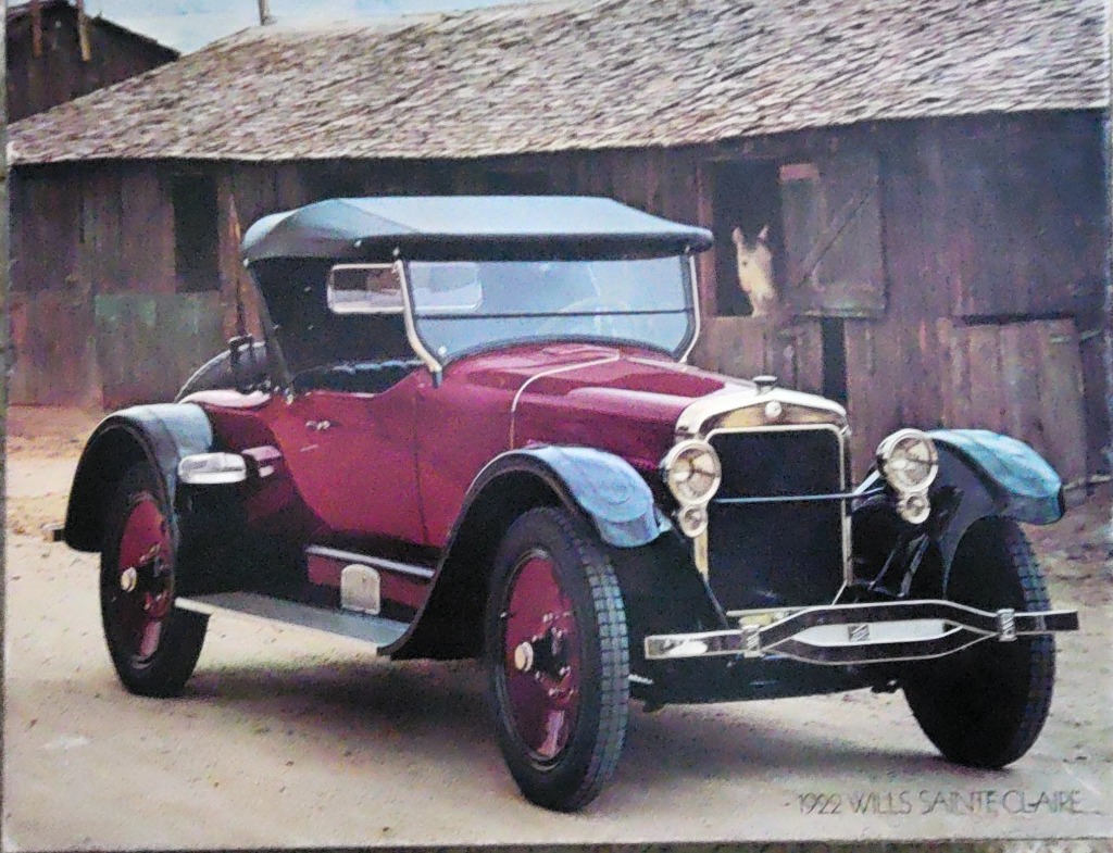 A vintage 1922 Wills Sainte Claire automobile parked in front of a rustic wooden barn.