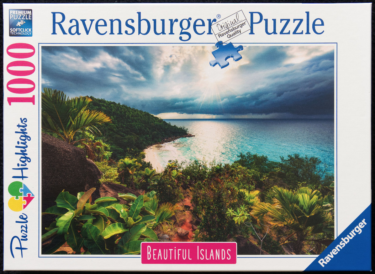 Tropical beach landscape featuring lush green hills, turquoise water, and a dramatic storm-clouded sky at sunset.